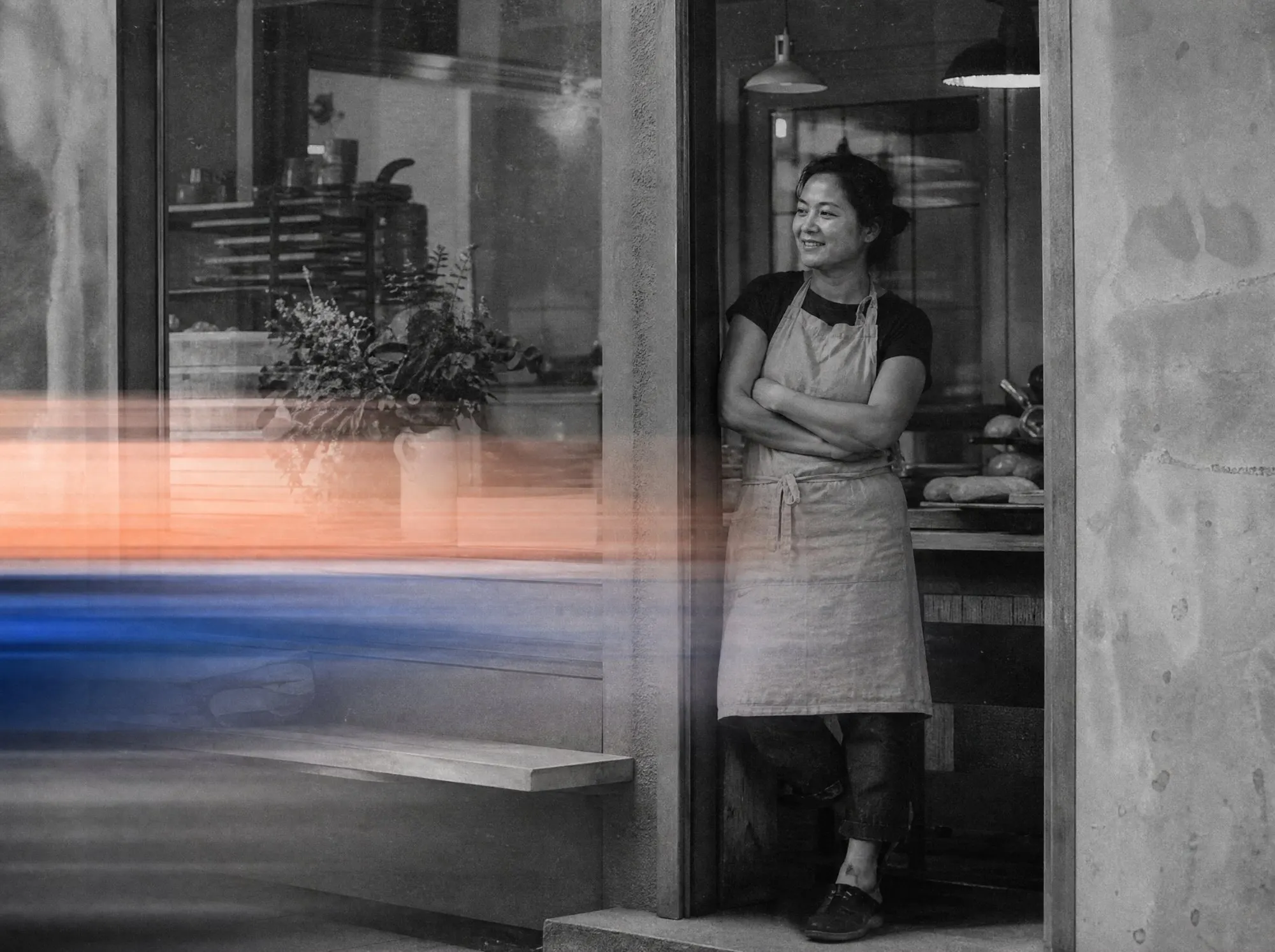 A bakery owner leaning in her shop doorway, arms crossed, smiling