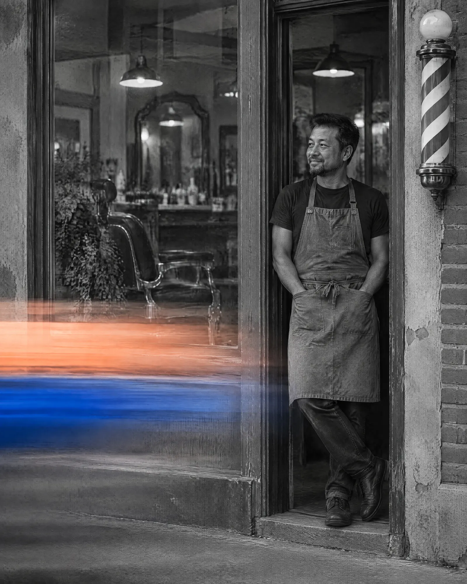 A barber leaning in the doorway of his shop, hands in his apron pockets