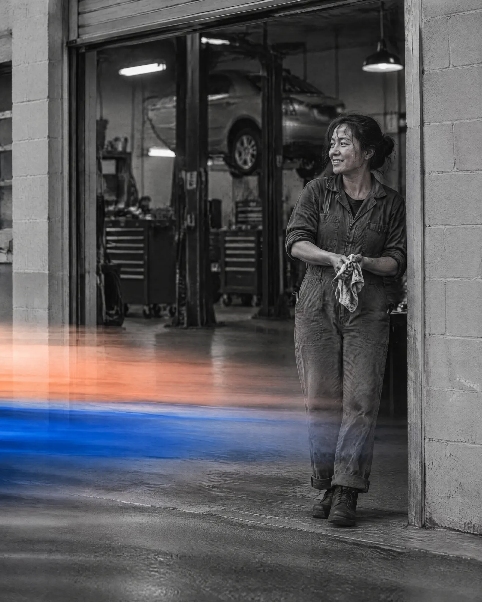 An auto mechanic in coveralls wiping her hands at the open door of her repair garage