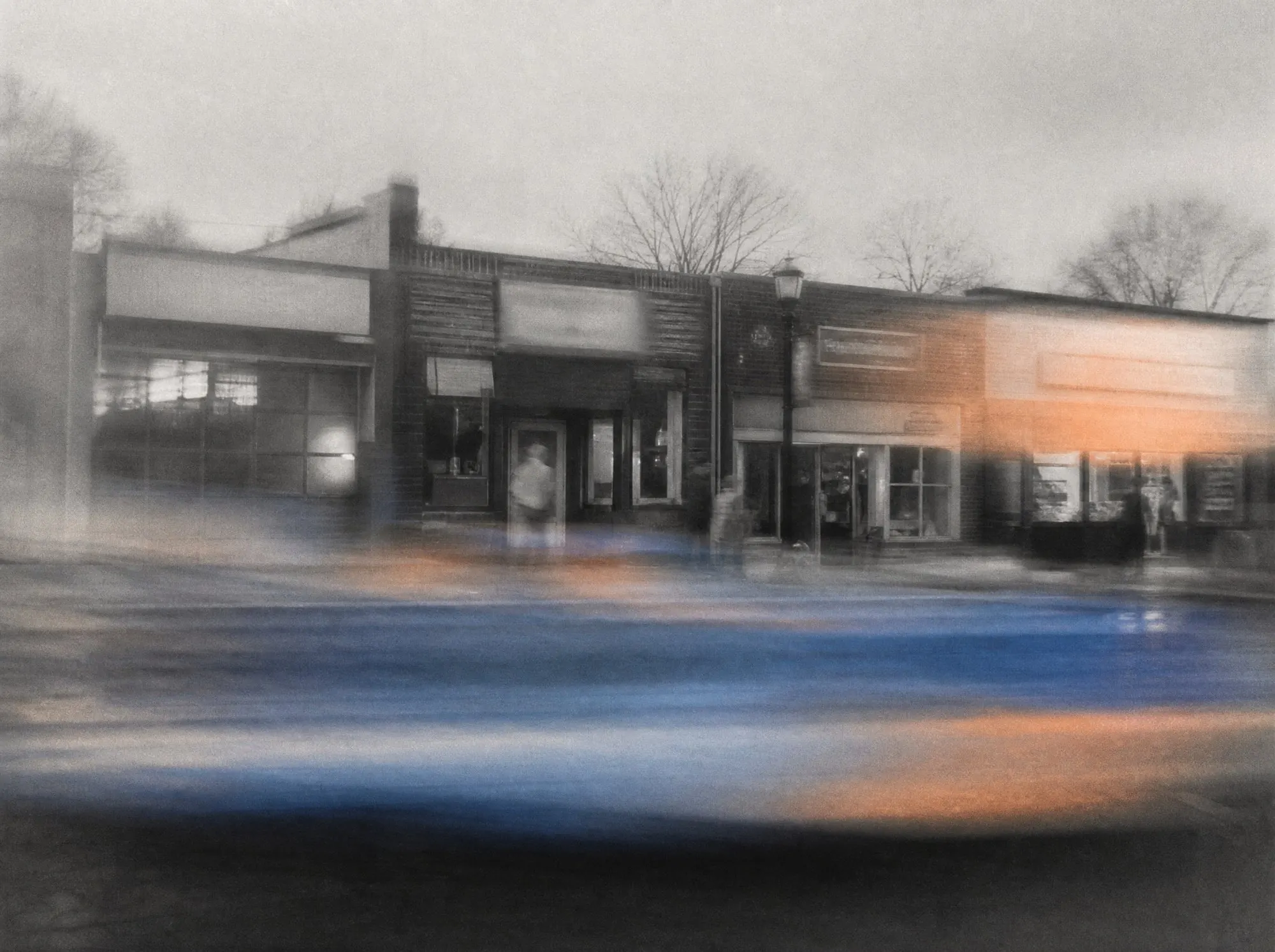 A row of independent storefronts on a small-town main street, blurred by passing traffic